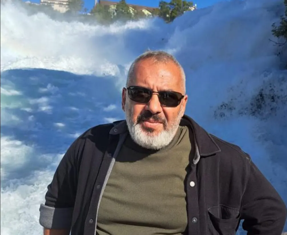 Ertuğrul Aslan Sezgin, güneş gözlüğü ve koyu ceketle bir şelalenin önünde